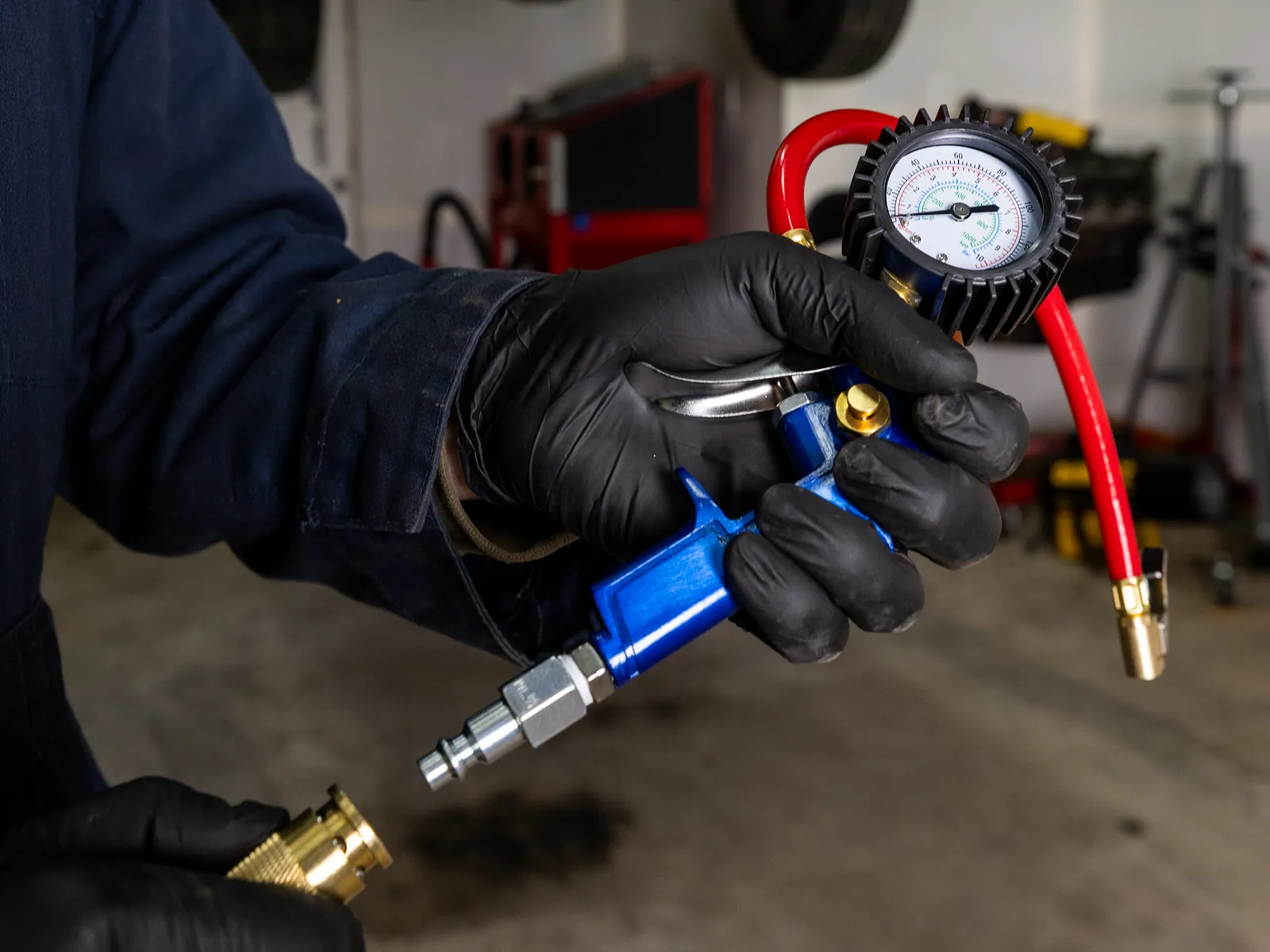 Gloved hand holding the 19344 tire inflator and dial gauge, with its red hose and brass air chuck